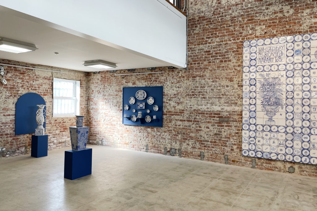 Exhibition photo at LBMA Downtown shows Elyse Pignolet's blue and white ceramic works: 2 vessels sit on cobalt blue platforms, and two installations are hung vertically on a brick wall.